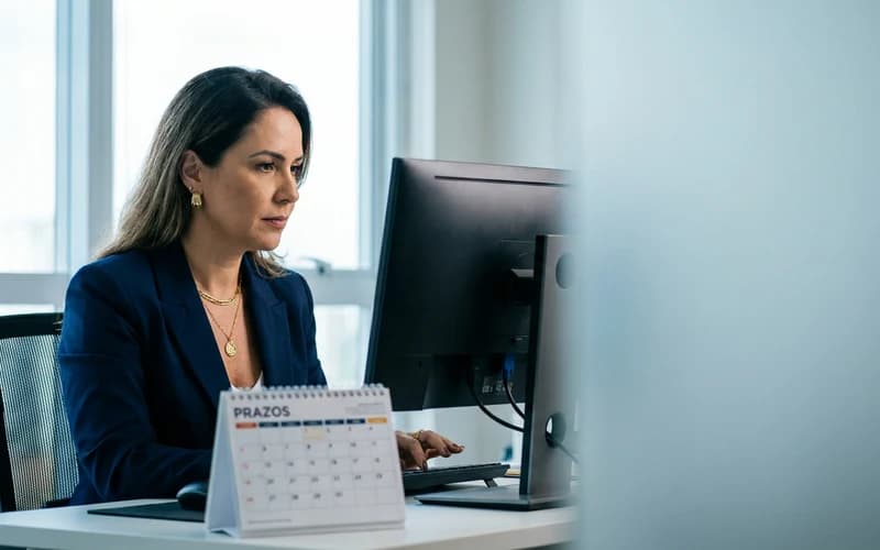 Profissional trabalha no computador com um calendário de prazos sobre a mesa do escritório